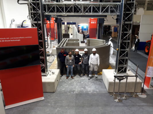 Mitarbeiter vor fertigem Haus auf der Bautec 2020