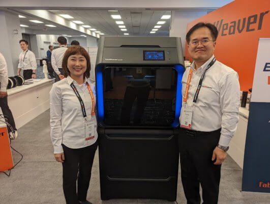 3D-Drucker und zwei Mitarbeiter des Unternehmens auf AMUG 2022