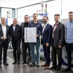 Verantwortliche stehen mit Zertifikat vor 3D-Drucker