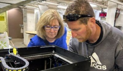 Dr. Nita Shattuck und Soldat betrachten 3D-Druckvorgang auf USCGC Healy Dr. Nita Shattuck und ein Soldat schauen in einen 3D-Drucker während einer Arktis-Expedition.