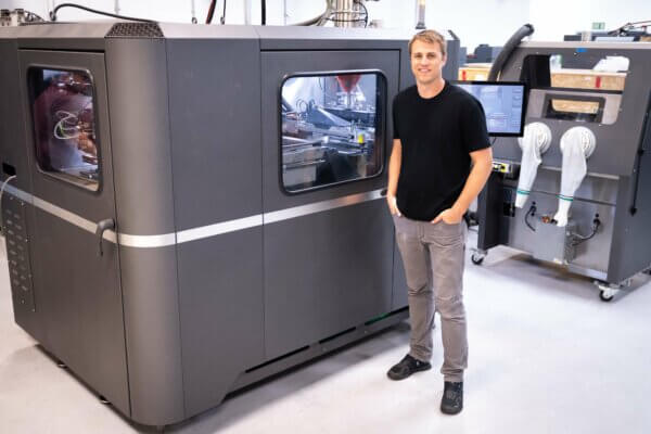 Nate Higgins vor dem Desktop Metal X25 Pro 3D-Drucker Nate Higgins neben einem X25 Pro 3D-Drucker von Desktop Metal