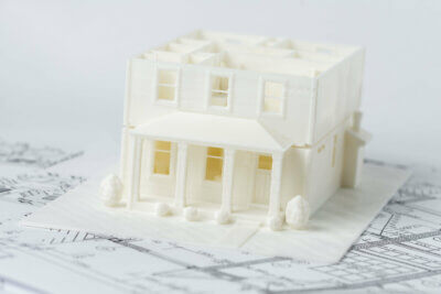 3D-gedrucktes Haus Modell mit ISO/ASTM 52939:2023 Standard auf Architektenplänen Miniatur 3D-gedrucktes Haus auf Plänen symbolisiert ISO/ASTM 52939:2023 Norm im Bauwesen