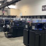 Innenansicht der 3D-Druckfarm in Nordtexas mit Reihen von aktiven 3D-Druckern und technischem Personal