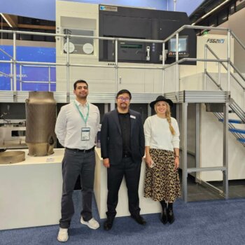Additive Plus und Farsoon Teams auf der Formnext 2023 neben einem 3D-Drucker Additive Plus und Farsoon Americas Vertreter bei Formnext, vor industrieller 3D-Drucktechnik