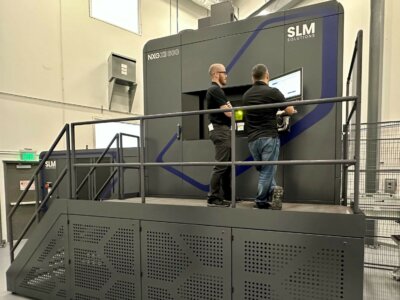 Techniker bedienen den SLM NXG XII 600 3D-Drucker bei Sintavia Zwei Mitarbeiter konfigurieren einen großen SLM NXG XII 600 3D-Drucker bei Sintavia