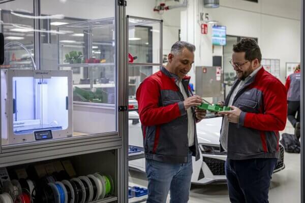 Audi Sport Mitarbeiter mit 3D-gedruckten Werkzeugen für den Audi E-Tron GT Zwei Audi Sport Mitarbeiter betrachten 3D-gedruckte Werkzeuge neben einem Ultimaker S5 3D-Drucker