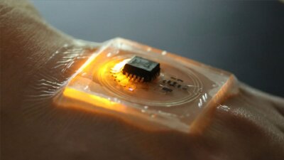 Tragbarer batterieloser Temperatursensor hergestellt mit CHARM3D-Technik Nahaufnahme eines tragbaren batterielosen Temperatursensors auf einer menschlichen Hand, gefertigt mit der CHARM3D-Technik der NUS