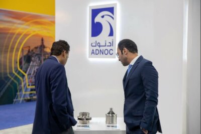 Adnoc Gas verwendet 3D-Druck zur Herstellung kritischer Ersatzteile und senkt dadurch Kosten und Emissionen. Zwei Mitarbeiter von Adnoc Gas betrachten 3D-gedruckte Ersatzteile an einem Messestand.