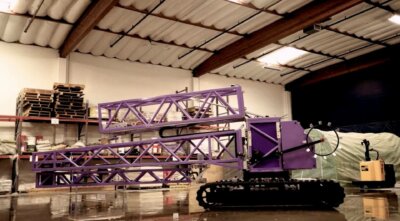 Transportabler 3D-Drucker D-Crafter von Contour Crafting in einer Werkshalle Transportabler 3D-Drucker D-Crafter von Contour Crafting in einer Werkshalle, violettfarbige Struktur und Kettenantrieb