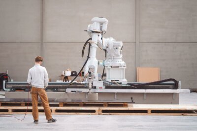 Techniker arbeitet mit einem Vertico 3D-Drucker für großformatige Betonstrukturen. Techniker neben einem Vertico 3D-Drucker für den Betonbau während des Druckprozesses.