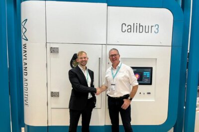 Tobias Neuwald und Wayland Additive vor dem Calibur3-Metalldrucker zur Erweiterung der 3D-Druck-Forschung. Tobias Neuwald vom Fraunhofer IPK und ein Vertreter von Wayland Additive stehen vor dem Calibur3-Metalldrucker, der auf der Formnext 2024 präsentiert wurde.