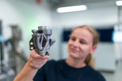 3D-gedrucktes Bauteil von TRUMPF für die Halbleiterindustrie zur Steigerung der Fertigungseffizienz Frau hält additiv gefertigtes Bauteil von TRUMPF zur Verbesserung der Halbleiterproduktion in der Hand