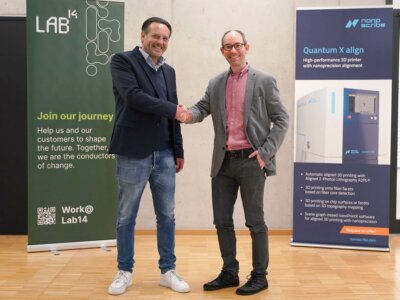 Martin Wynaendts van Resandt und Martin Hermatschweiler bei der Bekanntgabe der Nanoscribe-Integration in die Lab14 Group. Zwei CEOs, Martin Wynaendts van Resandt von Lab14 und Martin Hermatschweiler von Nanoscribe, schütteln sich die Hände vor Bannern mit Informationen zur Kooperation und 3D-Drucktechnologien.