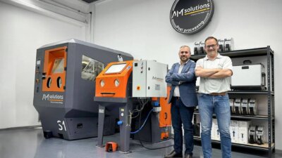 S1 Strahlanlage von AM Solutions im Einsatz bei Aitiip für automatisierte Nachbearbeitung Pablo Murillo und Xavier Pardo vor der S1 Strahlanlage von AM Solutions, verwendet für automatisierte Nachbearbeitungsprozesse bei Aitiip