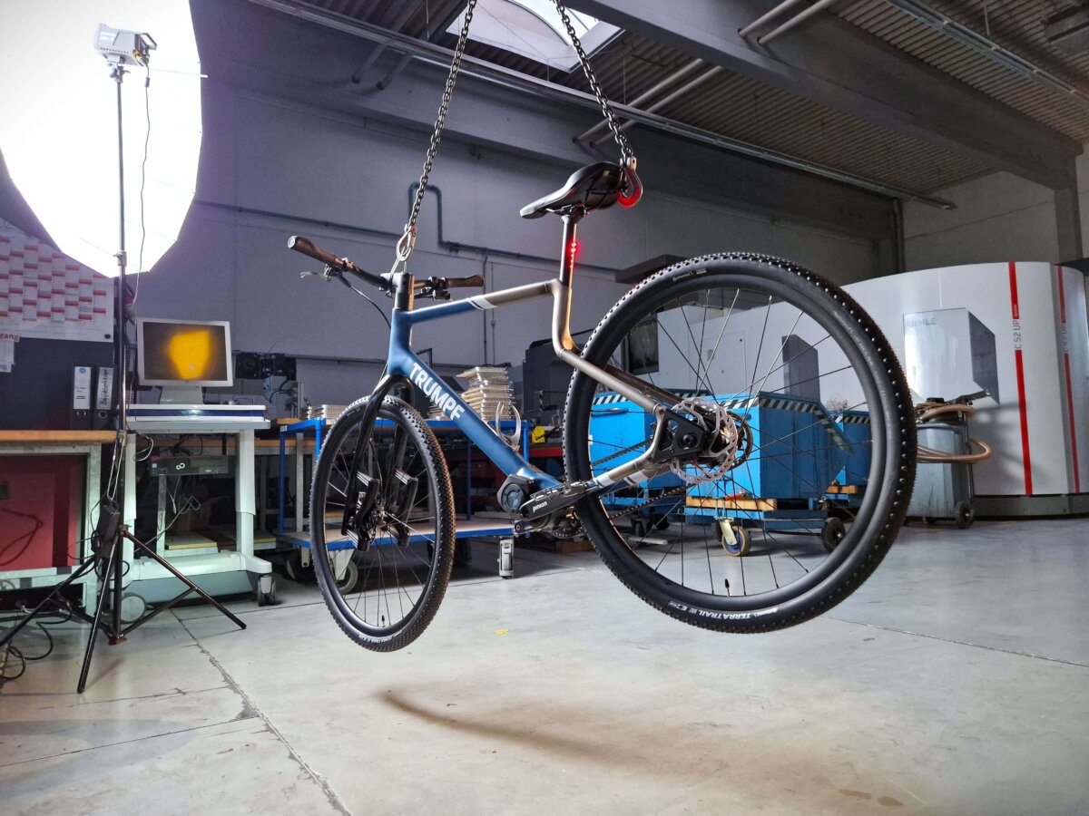 Hängendes Fahrrad mit 3D-gedrucktem Stahlrahmen von URWAHN in einer Werkstatt mit Maschinen im Hintergrund