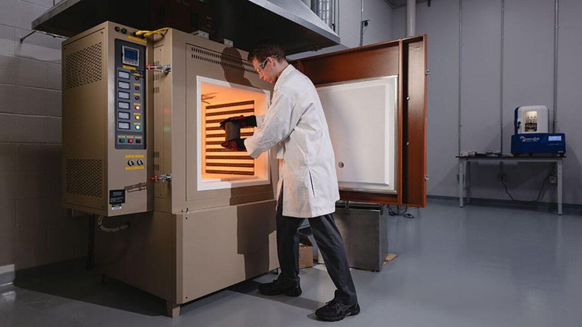 Ein Forscher legt eine 3D-gedruckte dunkle Keramikprobe in einen Hochtemperaturofen zur Materialverarbeitung für Hyperschallflugzeuge.