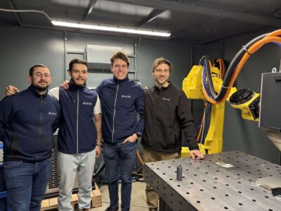 Team von ACNS und Meltio bei der Integration des Meltio Engine Blue in Roboter- und CNC-Systeme Teammitglieder von ACNS und Meltio in einer Produktionsumgebung mit Industrieroboter und 3D-Drucksystem