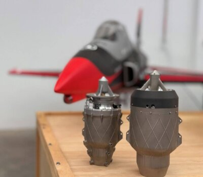 Zwei Mikrogasturbinen von Aurora Labs, Modell AU4 und AU2, nebeneinander aufgestellt vor einem UAV-Modell, entwickelt mit 3D-Drucktechnik für unbemannte Flugzeuge