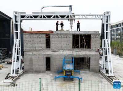 3D-Druck eines zweistöckigen Hauses in China mit großformatigem Betondrucker Bau eines zweistöckigen Hauses in China mit 3D-Drucker aus Beton, Arbeiter auf dem Dach, Portalrahmen-Drucksystem sichtbar