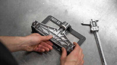 Hände halten eine 3D-gedruckte Vorrichtung zur präzisen Positionierung eines Bauteils neben einem digitalen Messschieber