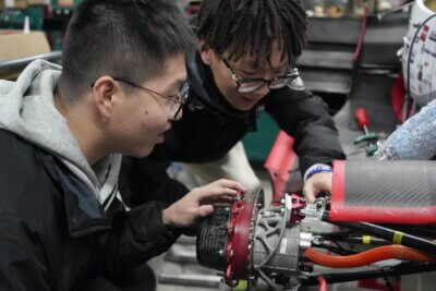 Zwei Ingenieure analysieren ein metallisches Motorsport-Bauteil, das mit einem 3D-Drucker von BLT gefertigt wurde