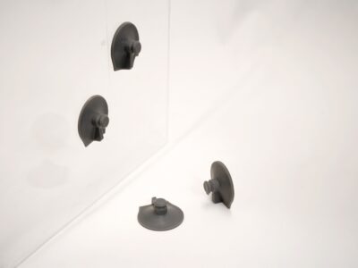 Vier schwarze 3D-gedruckte Saugnäpfe aus P3 Silicone 25A, zwei davon haften an einer transparenten Fläche, zwei liegen daneben auf weißem Untergrund