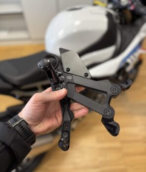 Hand hält 3D-gedrucktes Prüfwerkzeug von Gilles Tooling vor Motorrad