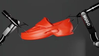 Roter 3D-gedruckter Schuh von Hugo Boss und Zellerfeld, gehalten von zwei schwarzen Roboterarmen